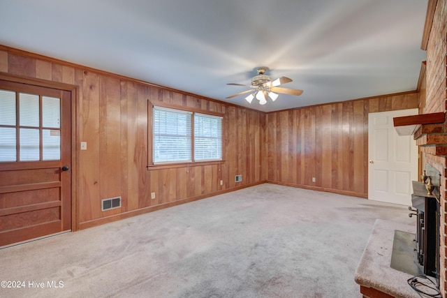 unfurnished living room with ceiling fan, a large fireplace, light colored carpet, and wooden walls