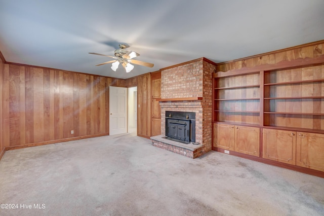 unfurnished living room featuring ceiling fan, light colored carpet, a fireplace, and wooden walls