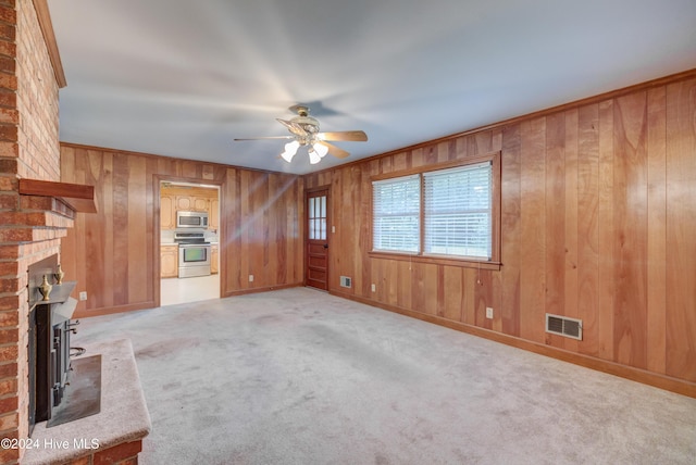 unfurnished living room featuring light carpet, a brick fireplace, ceiling fan, and wood walls