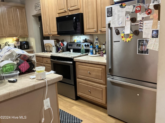 kitchen with tile counters, light hardwood / wood-style floors, light brown cabinets, and appliances with stainless steel finishes