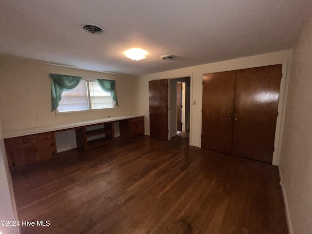 unfurnished bedroom with dark hardwood / wood-style flooring and built in desk