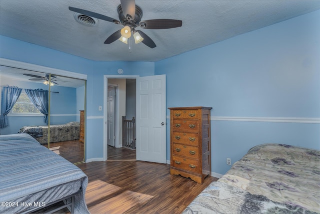 bedroom with ceiling fan, dark hardwood / wood-style flooring, a textured ceiling, and a closet