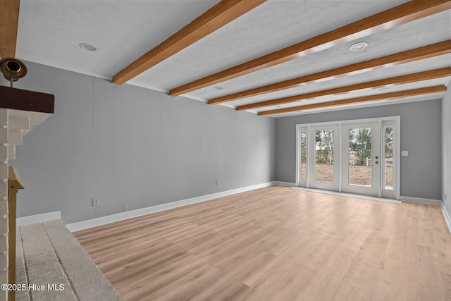 unfurnished living room with beamed ceiling, light hardwood / wood-style floors, and a textured ceiling