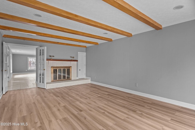 unfurnished living room featuring a fireplace, beamed ceiling, light hardwood / wood-style floors, and french doors