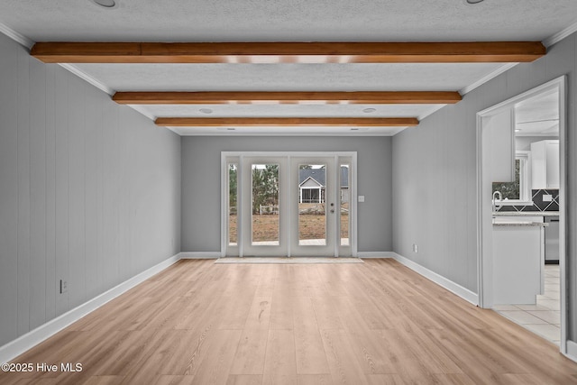 unfurnished living room featuring a textured ceiling, light wood-type flooring, and beam ceiling