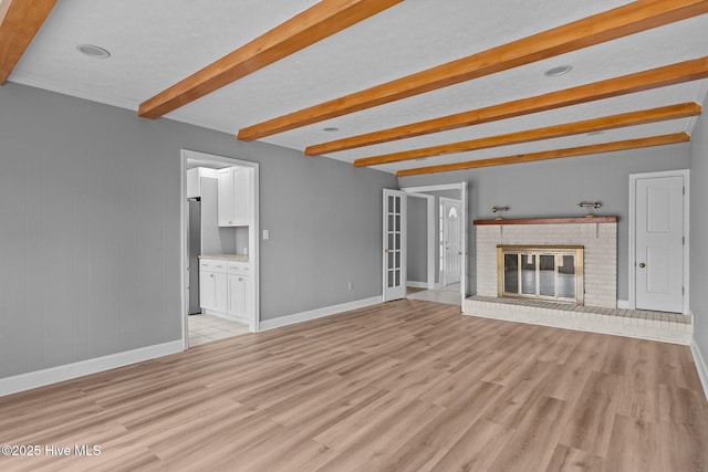 unfurnished living room featuring beam ceiling, light hardwood / wood-style flooring, and a brick fireplace