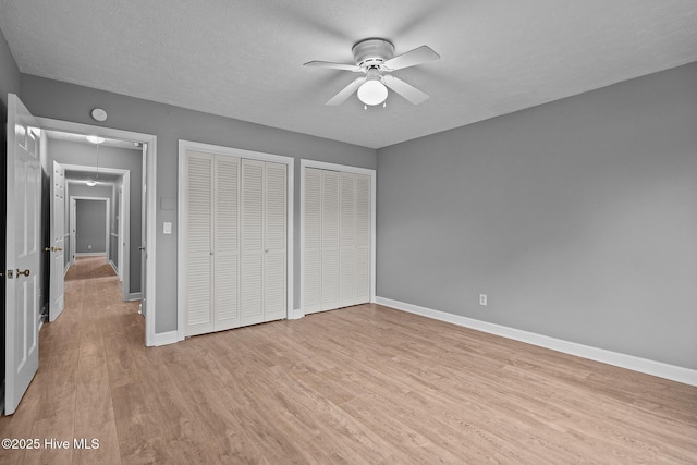 unfurnished bedroom with ceiling fan, light hardwood / wood-style floors, a textured ceiling, and multiple closets