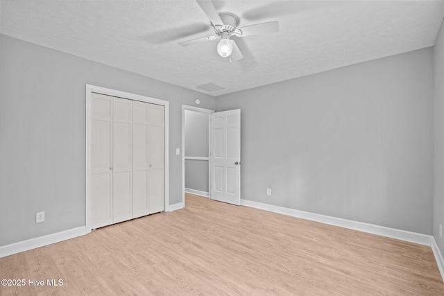 unfurnished bedroom featuring a textured ceiling, a closet, light hardwood / wood-style flooring, and ceiling fan