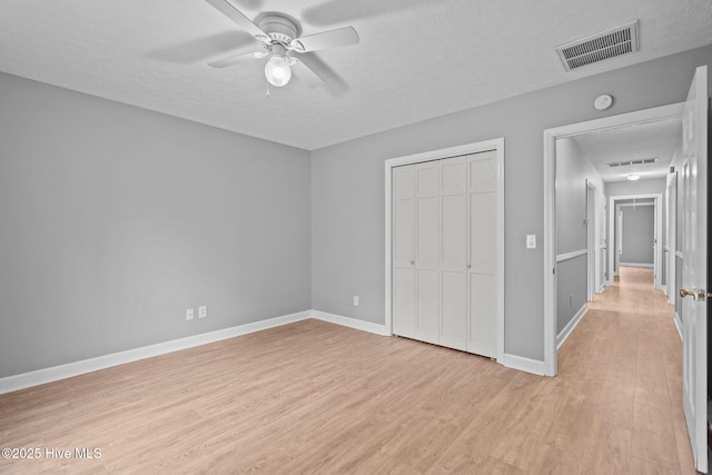 unfurnished bedroom featuring ceiling fan, a closet, a textured ceiling, and light wood-type flooring