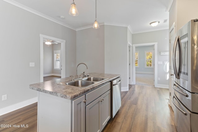 kitchen with gray cabinetry, stainless steel appliances, sink, decorative light fixtures, and an island with sink