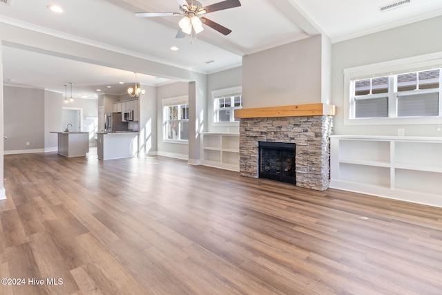 unfurnished living room featuring ceiling fan with notable chandelier, light hardwood / wood-style floors, a stone fireplace, and crown molding