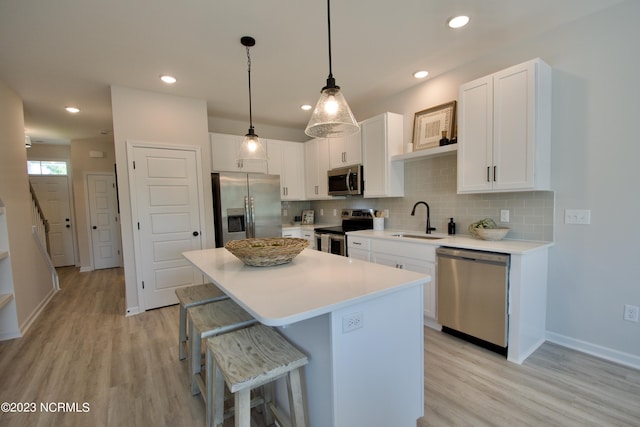 kitchen featuring light wood-type flooring, stainless steel appliances, sink, a center island, and white cabinetry