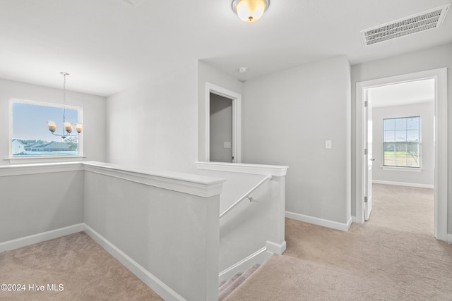 hallway with light colored carpet and an inviting chandelier