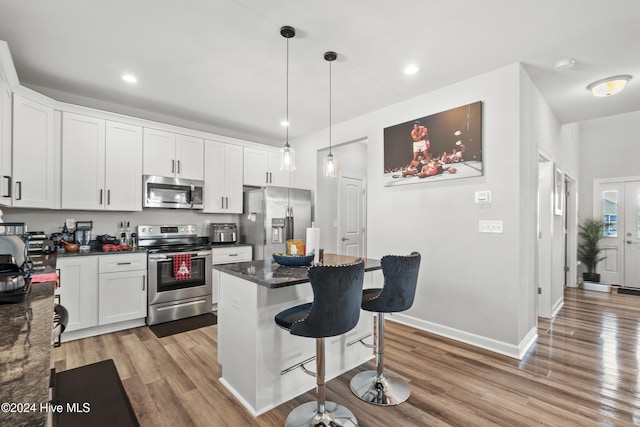 kitchen with white cabinets, light wood-type flooring, decorative light fixtures, a kitchen island, and stainless steel appliances