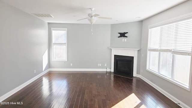 unfurnished living room with ceiling fan, dark wood-type flooring, and a wealth of natural light