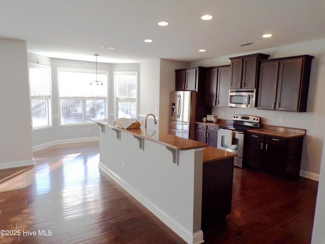 kitchen with appliances with stainless steel finishes, a breakfast bar, decorative light fixtures, dark hardwood / wood-style floors, and an island with sink