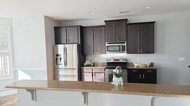 kitchen featuring appliances with stainless steel finishes, dark brown cabinets, and a breakfast bar area