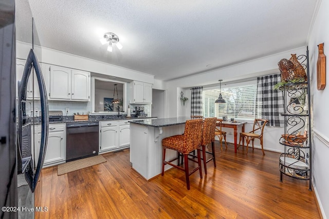 kitchen featuring decorative backsplash, a kitchen breakfast bar, dark wood-type flooring, black appliances, and white cabinetry