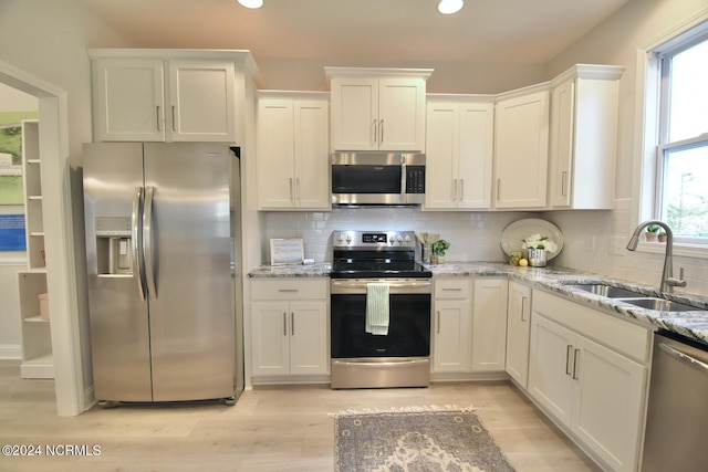 kitchen featuring stainless steel appliances, tasteful backsplash, light wood-style flooring, white cabinets, and a sink