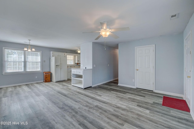 unfurnished living room featuring ceiling fan with notable chandelier and light hardwood / wood-style floors