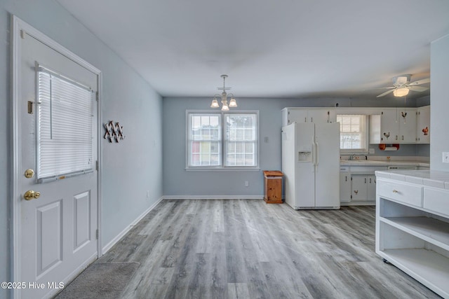 kitchen with white cabinetry, tile counters, white fridge with ice dispenser, hanging light fixtures, and ceiling fan with notable chandelier