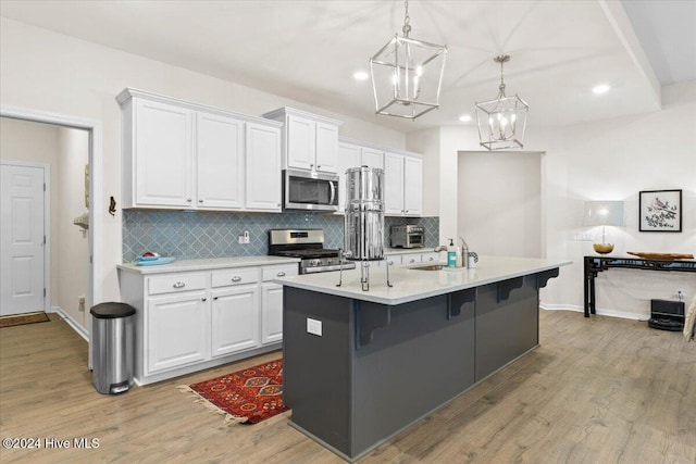 kitchen with white cabinetry, hanging light fixtures, appliances with stainless steel finishes, a kitchen breakfast bar, and an island with sink