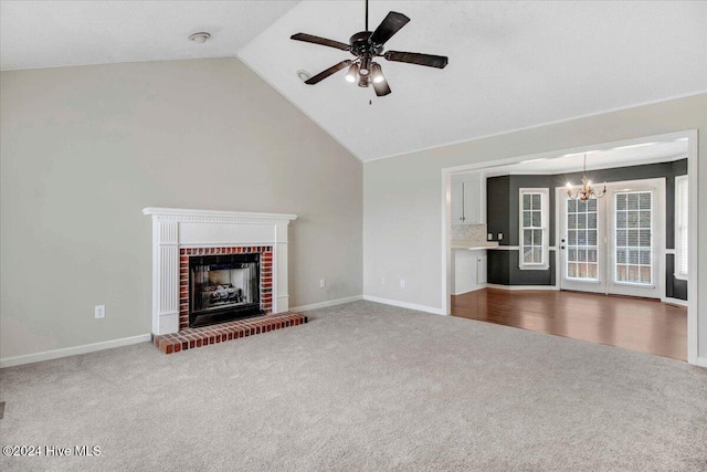 unfurnished living room featuring carpet flooring, ceiling fan with notable chandelier, a fireplace, and vaulted ceiling