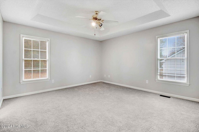 carpeted spare room featuring a tray ceiling, ceiling fan, and a textured ceiling