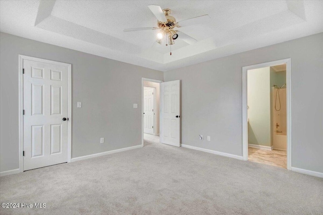 unfurnished bedroom featuring ceiling fan, a textured ceiling, connected bathroom, and a tray ceiling