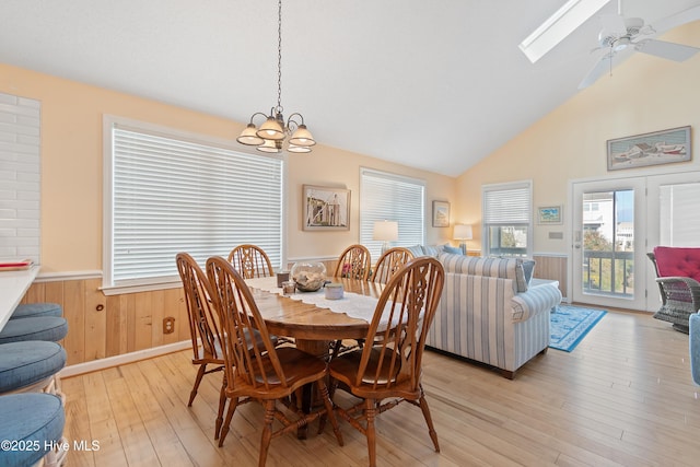 dining room featuring a skylight, light hardwood / wood-style flooring, high vaulted ceiling, and ceiling fan with notable chandelier