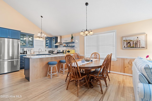 dining area featuring wood walls, light wood-type flooring, lofted ceiling, and an inviting chandelier