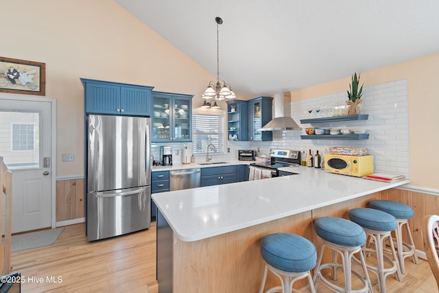 kitchen featuring sink, wall chimney range hood, blue cabinets, kitchen peninsula, and appliances with stainless steel finishes