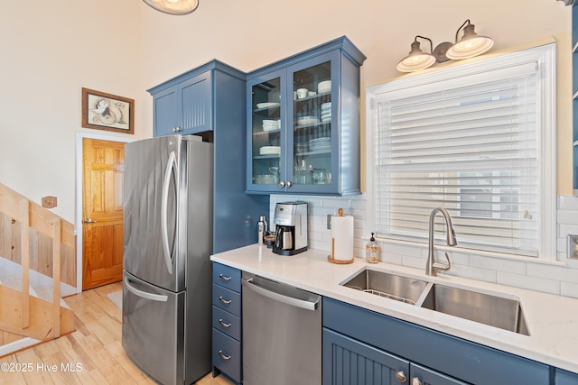 kitchen featuring decorative backsplash, appliances with stainless steel finishes, sink, blue cabinetry, and light hardwood / wood-style floors