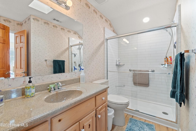 bathroom with a skylight, vanity, a shower with shower door, and toilet