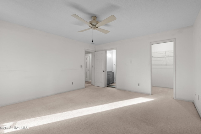 unfurnished bedroom with a closet, a walk in closet, light colored carpet, and ceiling fan