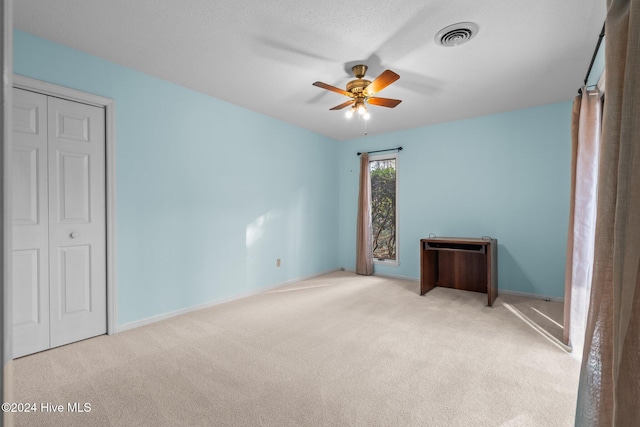 unfurnished bedroom featuring ceiling fan, a closet, light carpet, and a textured ceiling