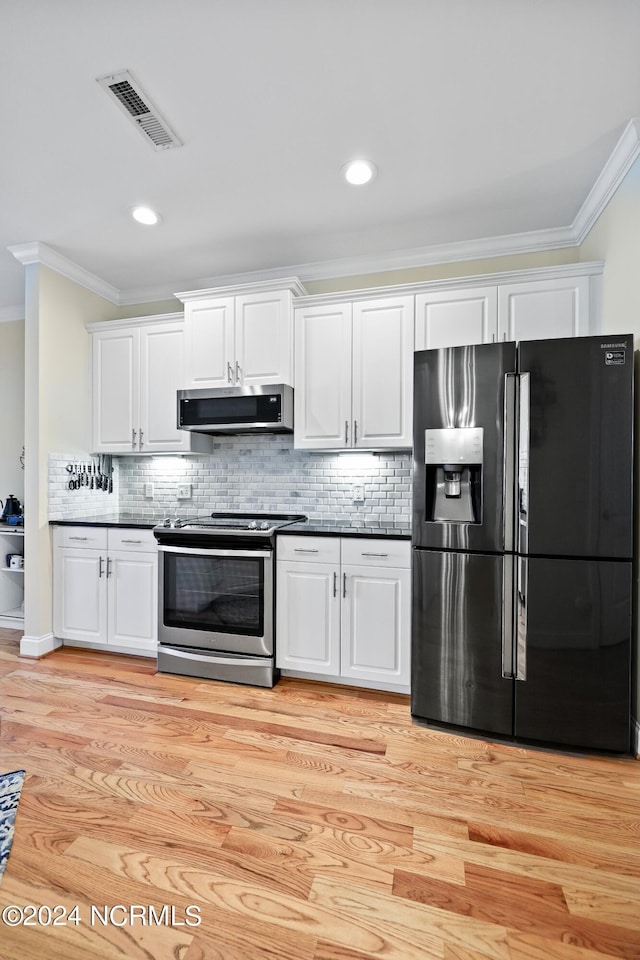 kitchen featuring stainless steel electric range oven, range hood, white cabinets, crown molding, and black fridge