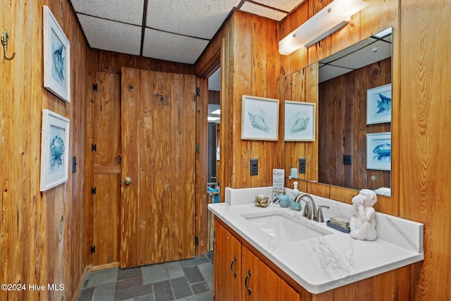 bathroom featuring a paneled ceiling, wooden walls, and vanity