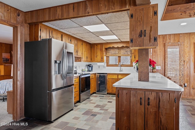 kitchen featuring sink, stainless steel appliances, wine cooler, kitchen peninsula, and wood walls