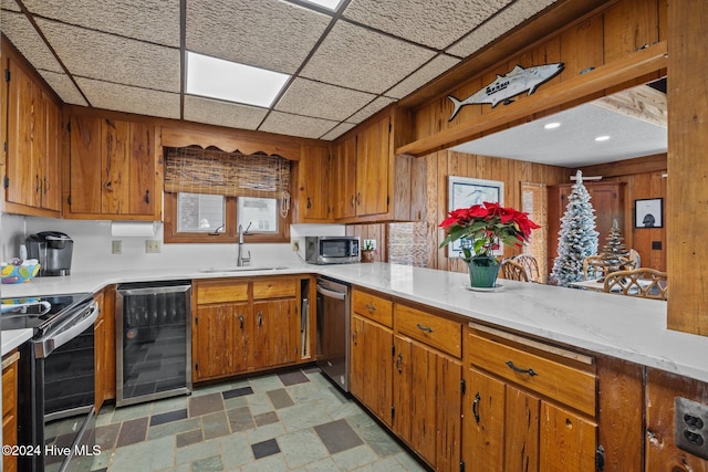 kitchen with appliances with stainless steel finishes, wood walls, sink, and wine cooler