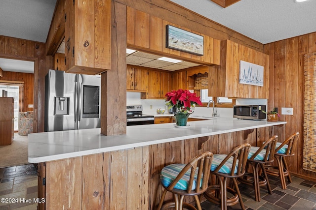 kitchen featuring kitchen peninsula, wooden walls, a textured ceiling, and appliances with stainless steel finishes