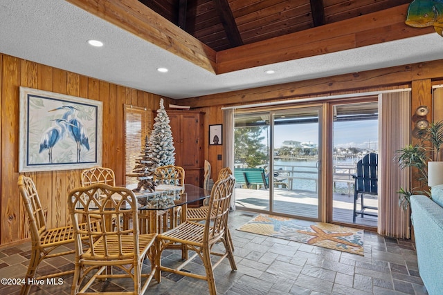 dining space with wooden walls, a water view, and a textured ceiling