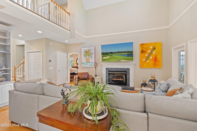 living room featuring wood-type flooring, a towering ceiling, and a tile fireplace