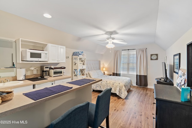 bedroom featuring ceiling fan, light hardwood / wood-style floors, sink, and vaulted ceiling