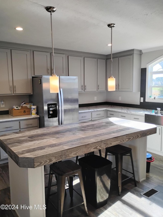 kitchen featuring wood counters, stainless steel fridge with ice dispenser, a center island, and a breakfast bar area