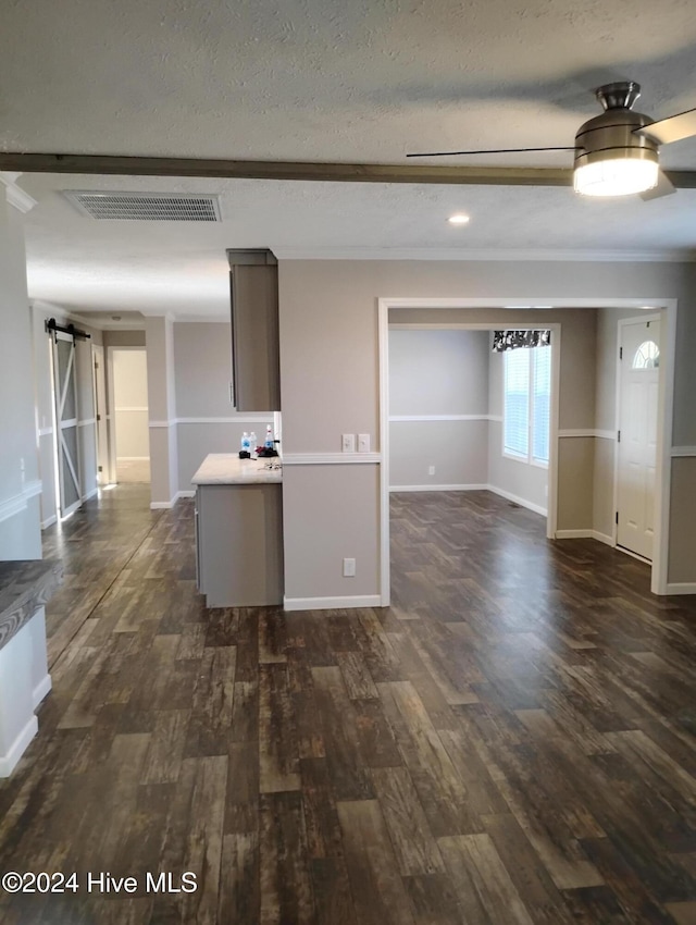 empty room with a textured ceiling, a barn door, crown molding, and dark wood-type flooring