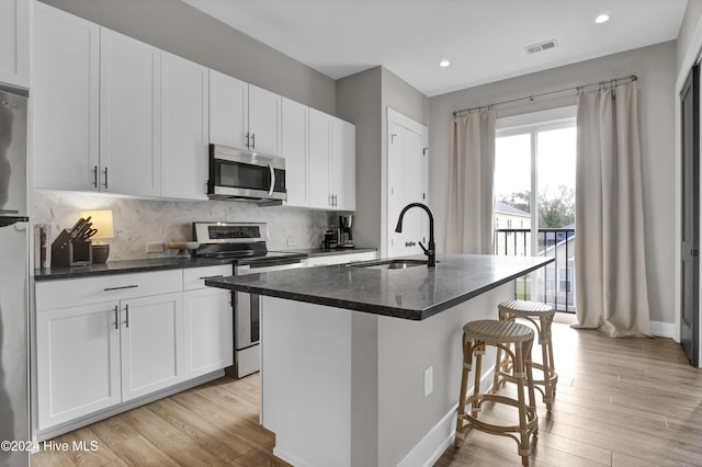 kitchen with appliances with stainless steel finishes, a center island with sink, white cabinetry, and sink