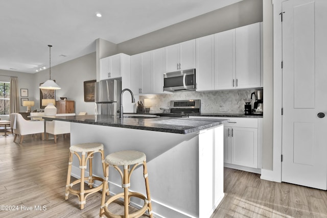 kitchen featuring a kitchen bar, stainless steel appliances, white cabinetry, and a kitchen island with sink