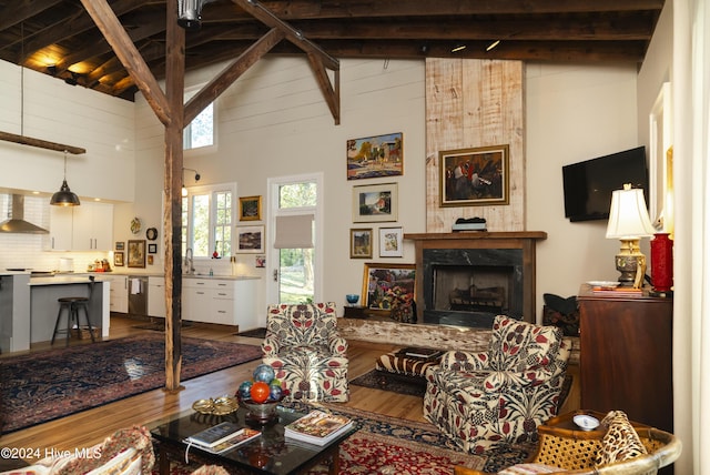 living room featuring high vaulted ceiling, sink, a fireplace, beamed ceiling, and wood-type flooring