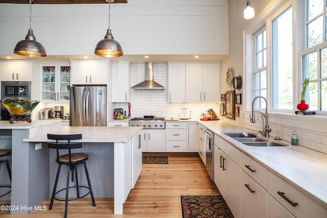 kitchen featuring pendant lighting, white cabinets, wall chimney range hood, sink, and appliances with stainless steel finishes